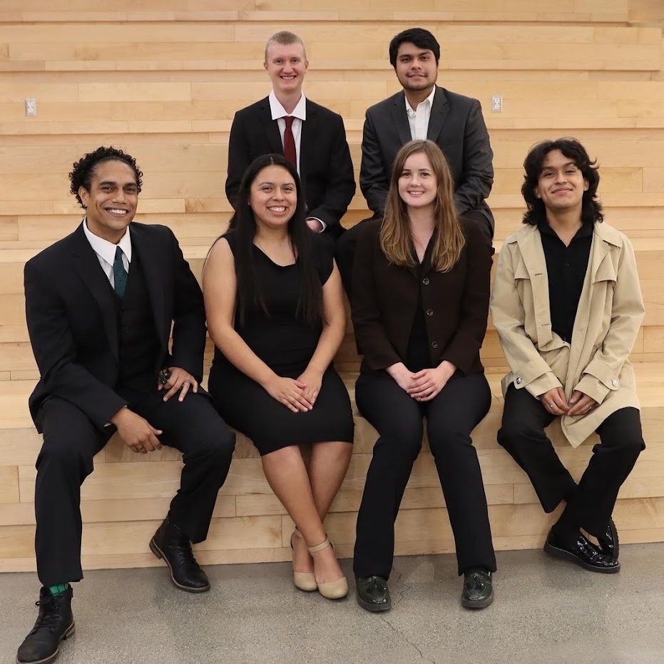 Six students in formal attire seated on a wooden bench at CSUF