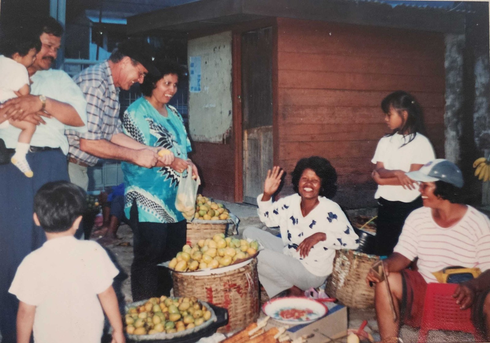 My mother buying fruit at a street market with German friends, the seller laughing and waving from behind her baskets
