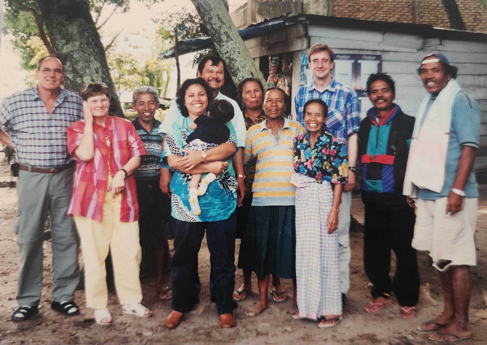 Eleven of us lined up for a photo outside a small wooden shop, my mother holding me