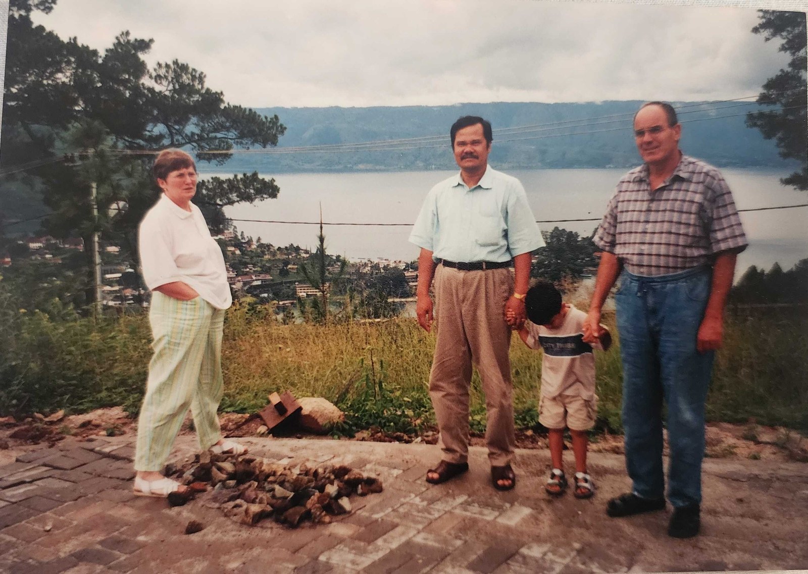 My dad holding my hand on a brick terrace above a wide lake, with a German couple standing either side of us