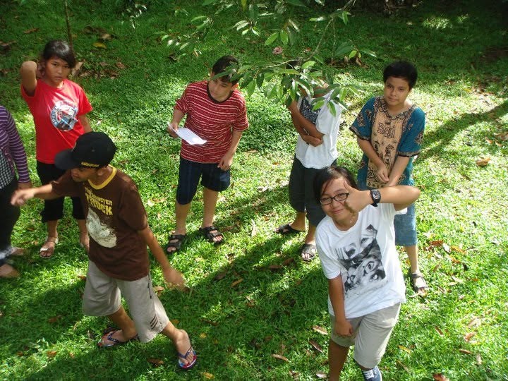 Standing around on the grass on a school trip, someone reading off a sheet of paper