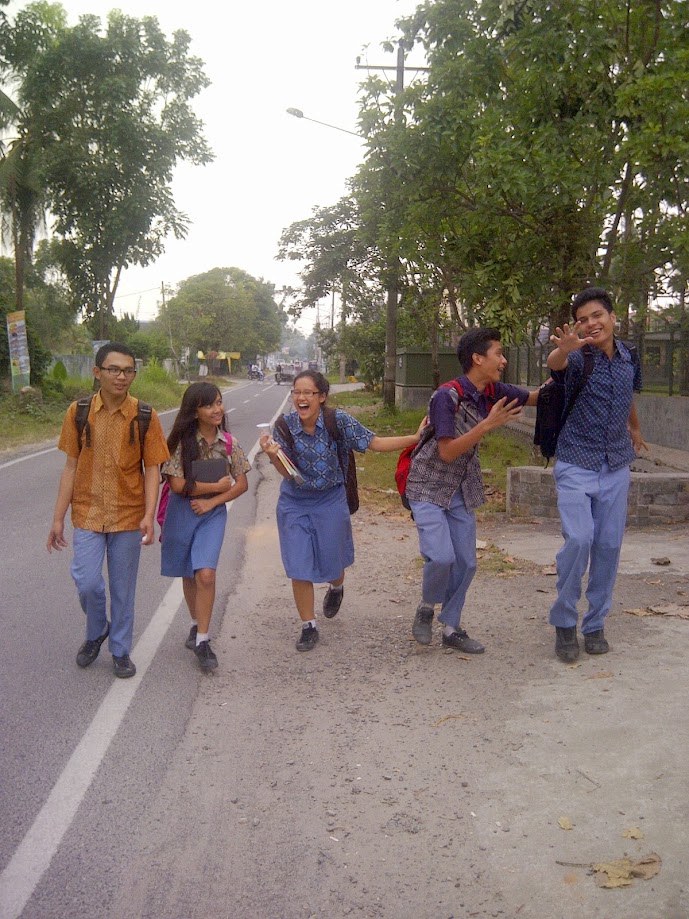 Five students in school uniform walking along a road, laughing