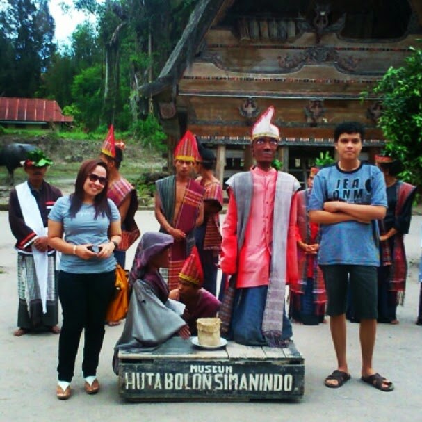 Standing beside traditional Batak figures at Museum Huta Bolon Simanindo