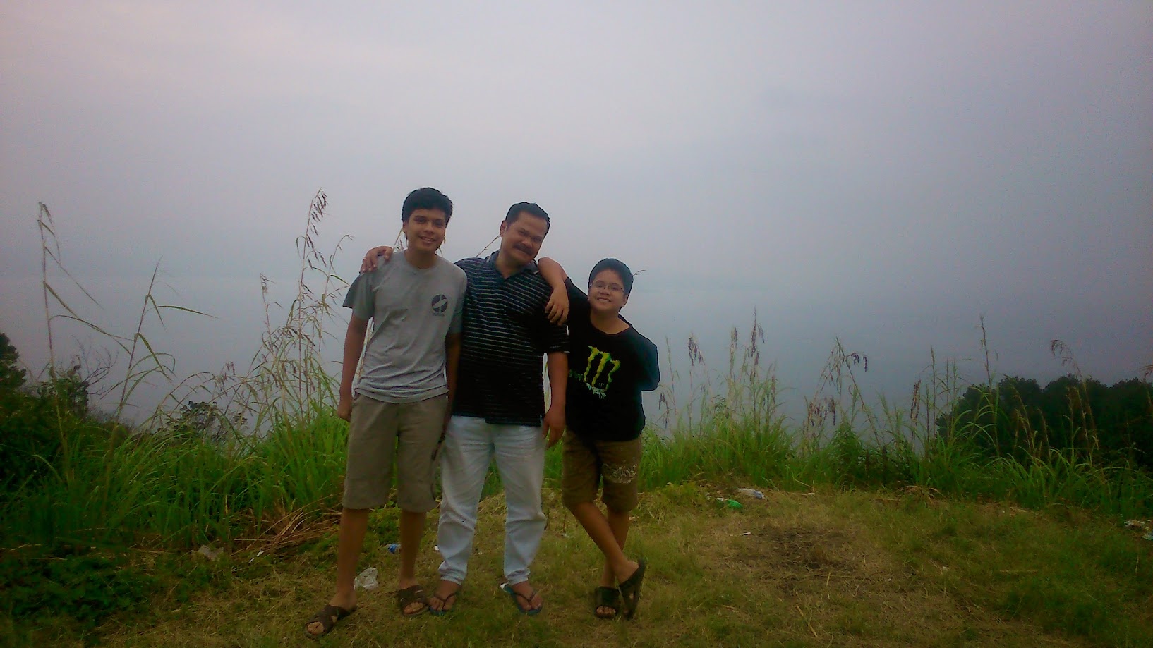 Three of us arm in arm on a grassy hilltop on a hazy day
