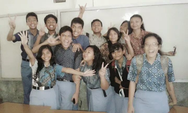Class group photo in batik uniforms, everyone throwing peace signs