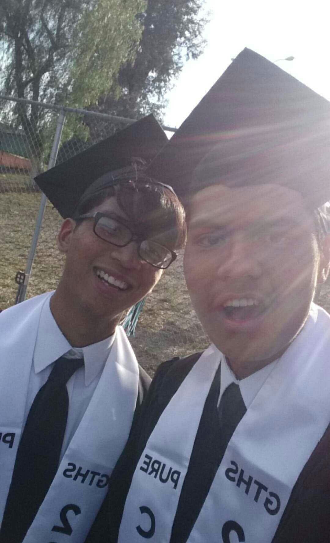Two of us in caps and gowns with our sashes on, high school graduation day