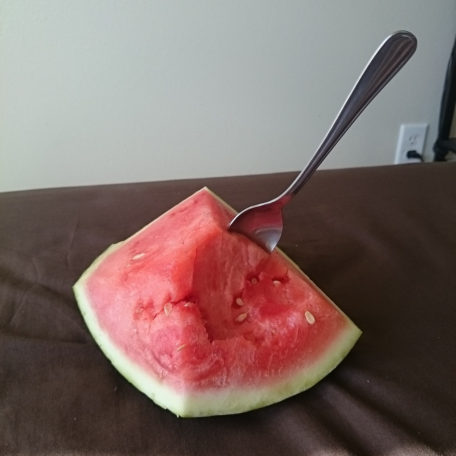 A wedge of watermelon on the table with a fork stuck straight into it