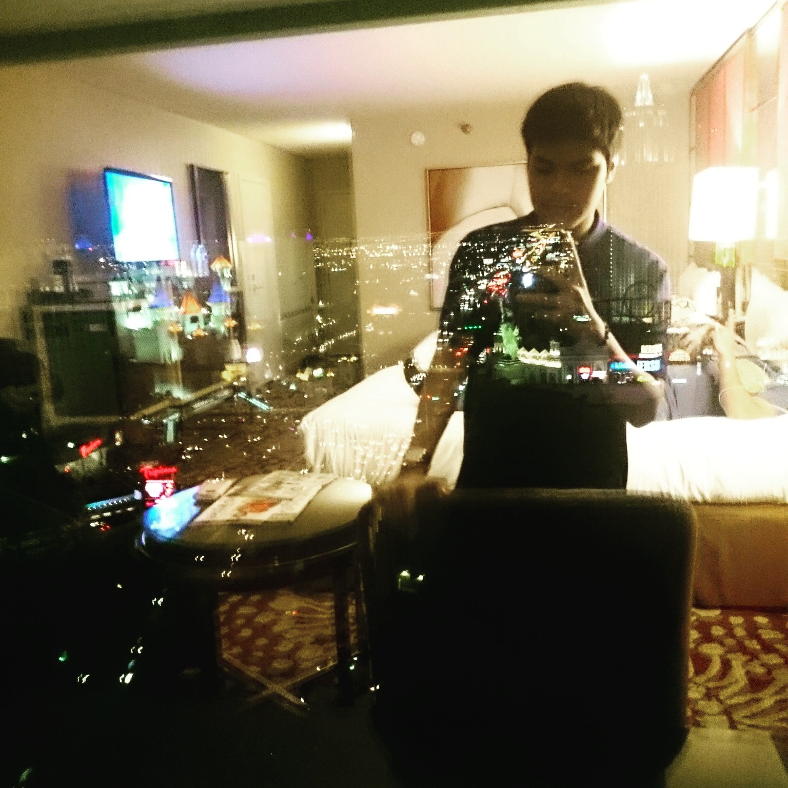 A hotel room at night reflected in the glass, city lights below