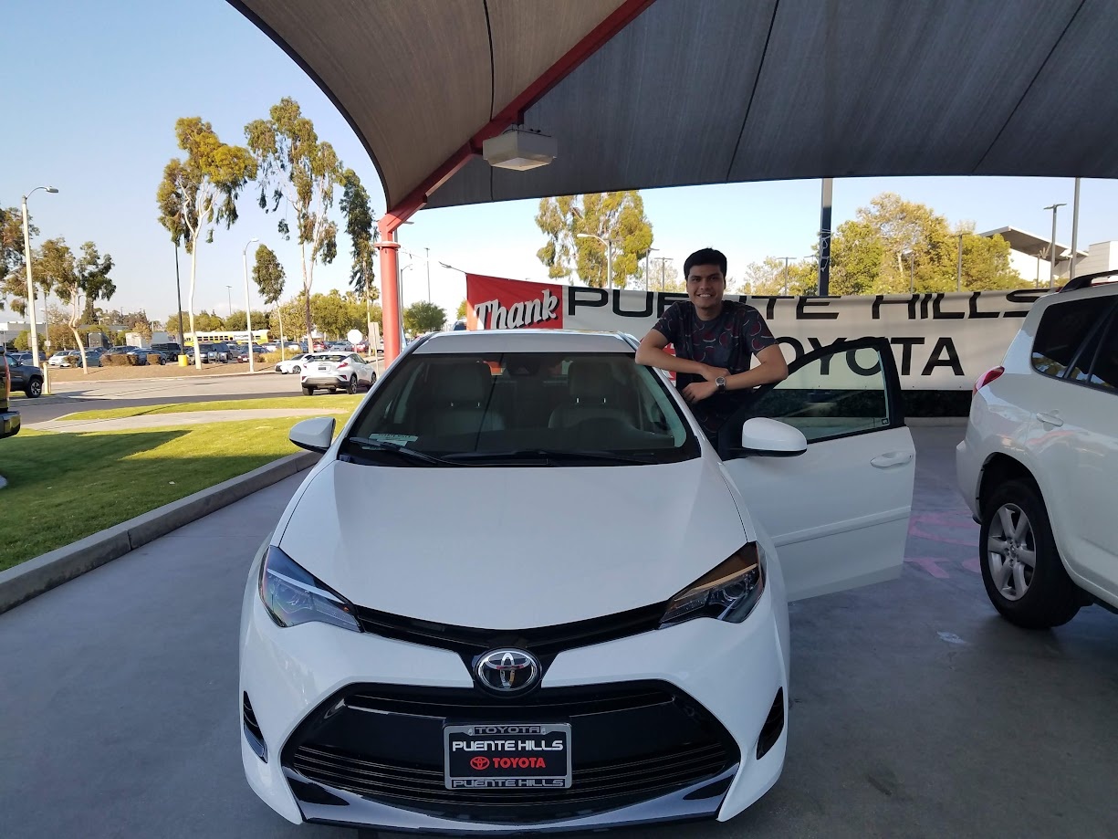 Standing beside my first car at the dealership, a white Toyota Corolla