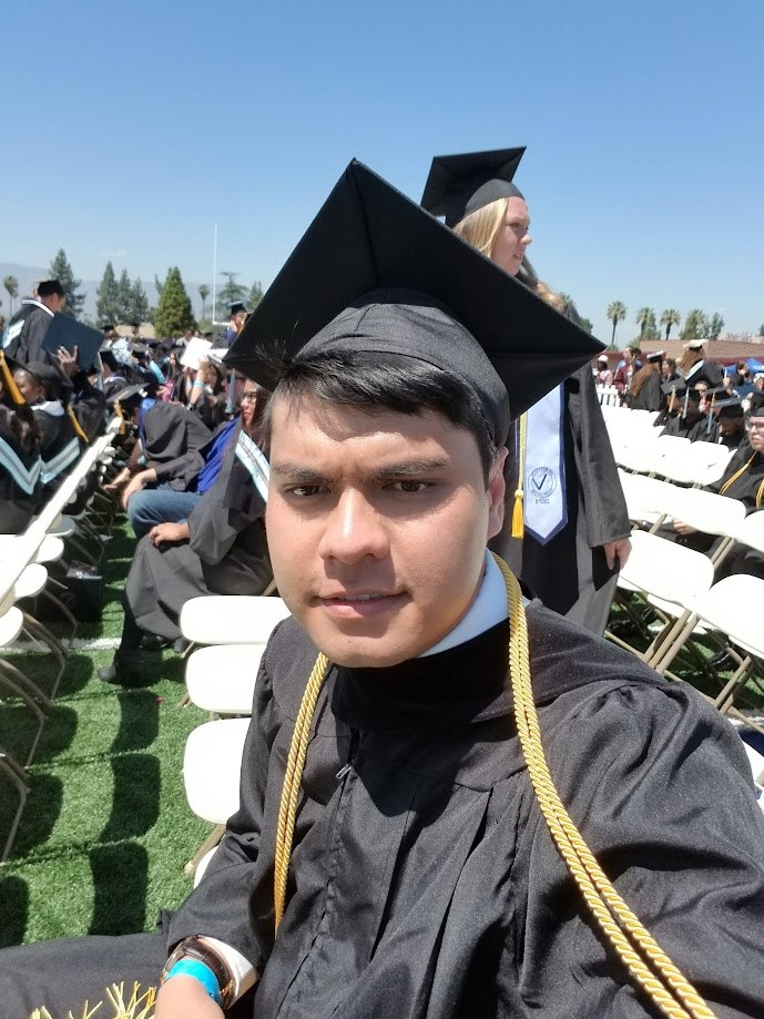Seated in cap and gown with honor cords at the graduation ceremony