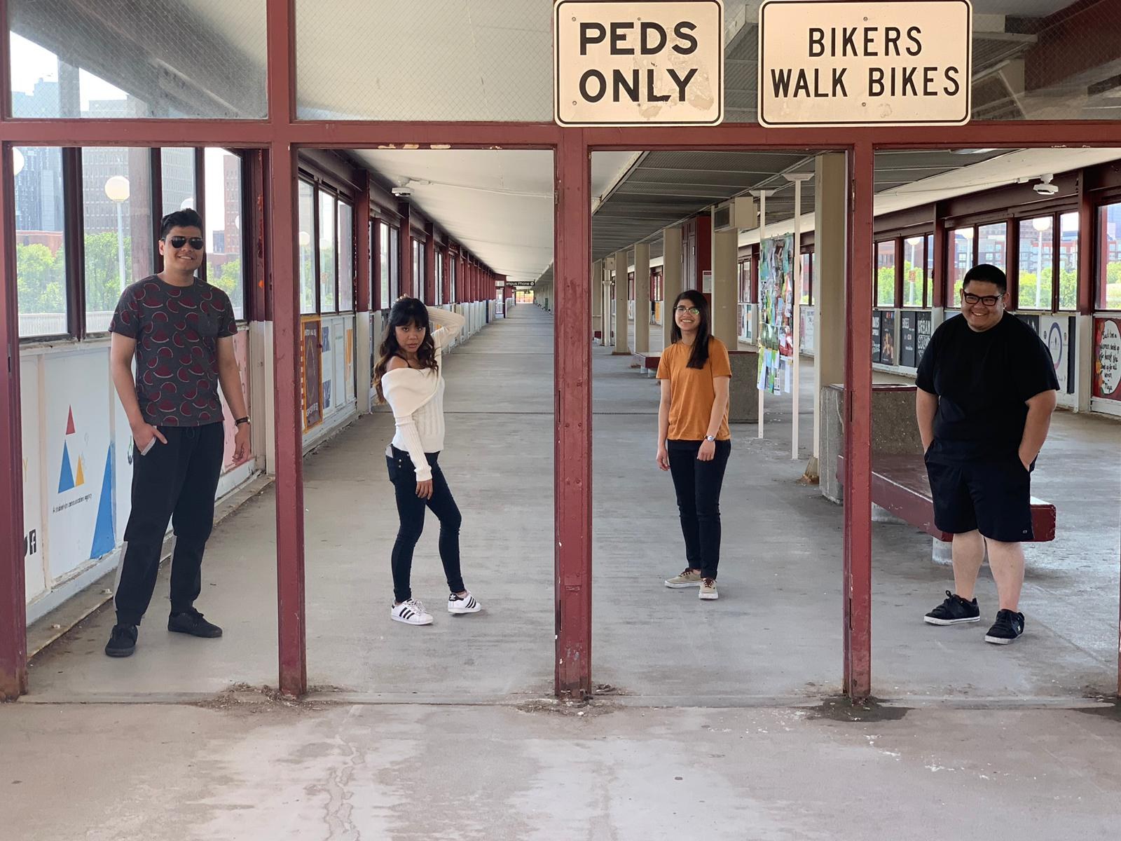 Four of us spaced out along a covered campus walkway under a Peds Only sign