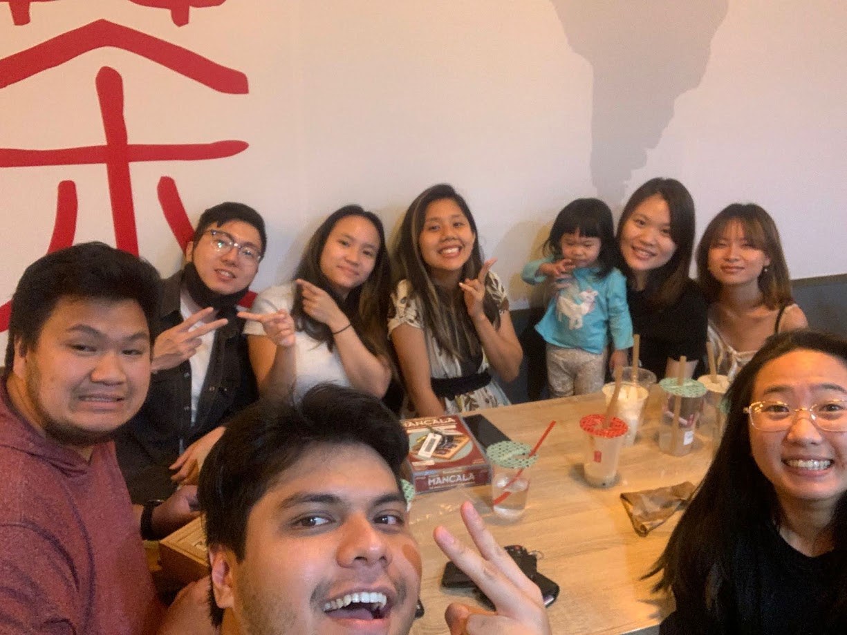 A long table of us at a boba shop, drinks everywhere and a Mancala board in the middle