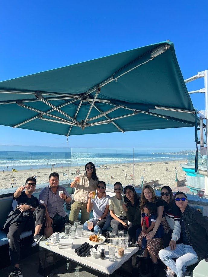 Group at a beachfront table under an umbrella with the surf behind