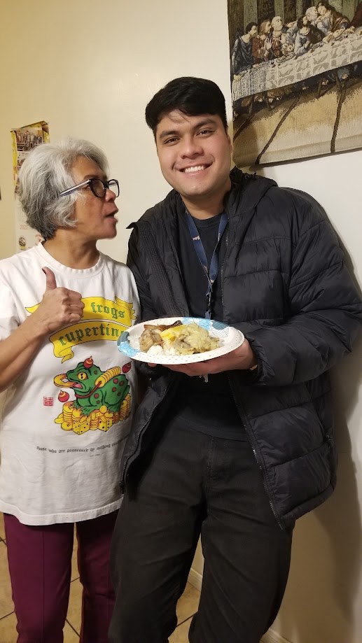 Holding a plate of my mother's cooking at home, she is giving it a thumbs up