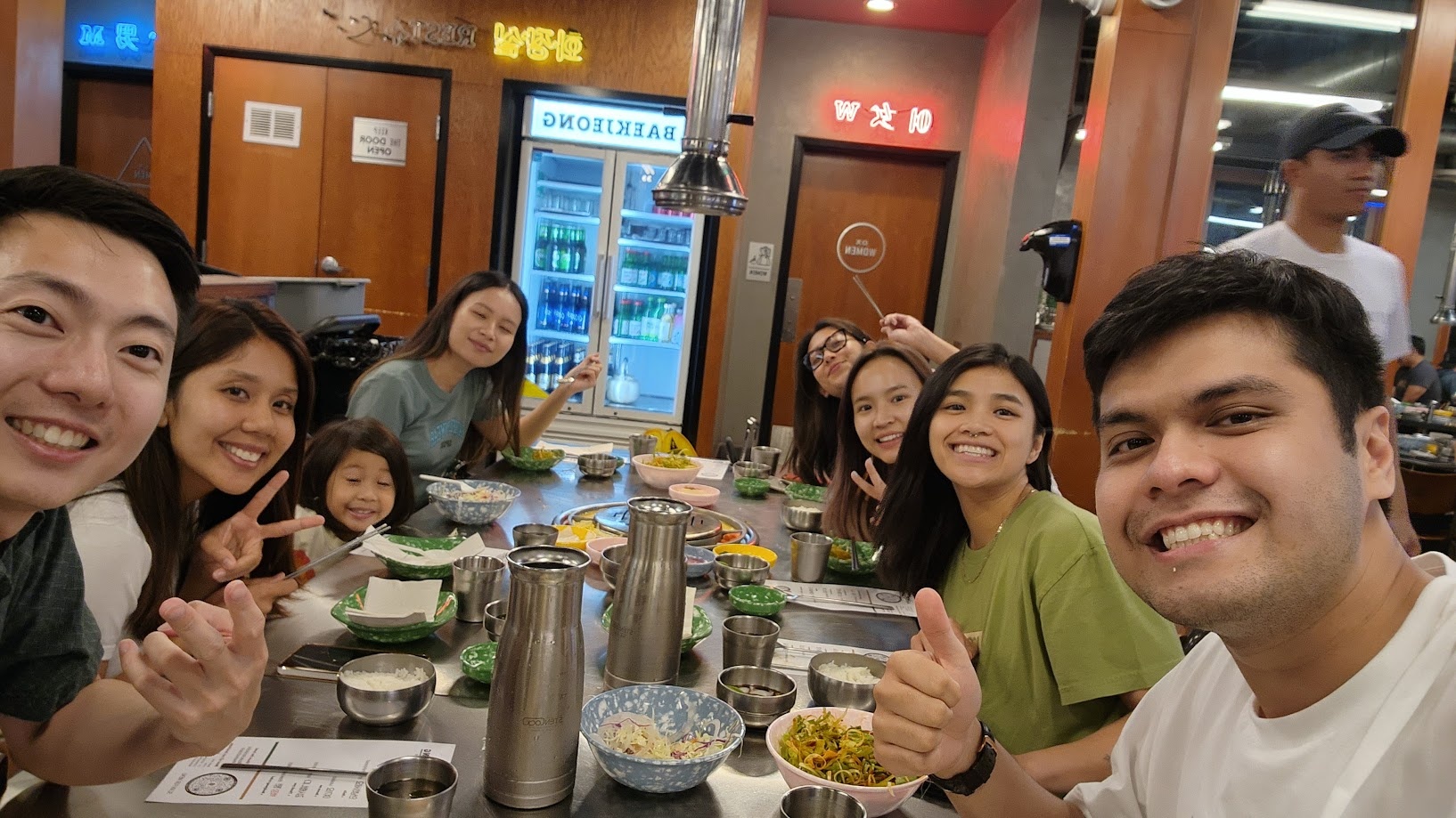 A long table of friends at Korean barbecue, everyone leaning in for the photo