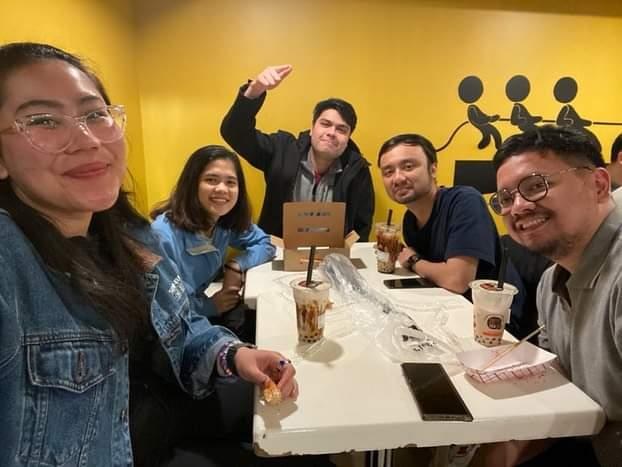Five of us around a small table at a boba shop with the yellow wall behind