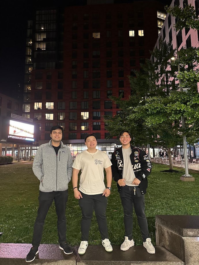 Three of us outside on the grass at night with the buildings lit behind