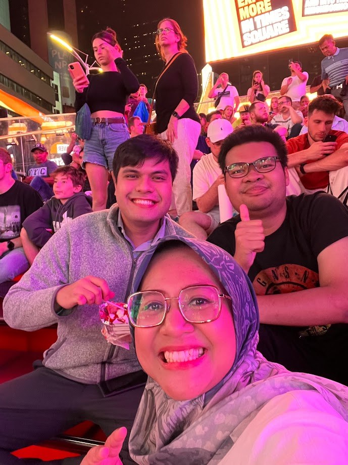 On the red steps in Times Square at night with the crowd behind