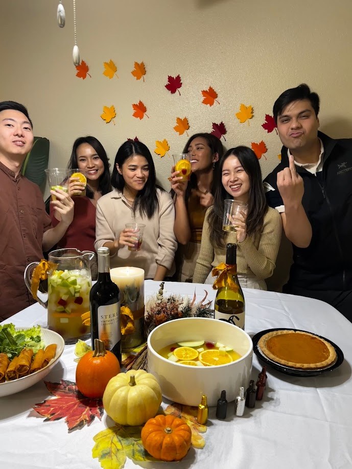 Friends raising glasses over a Thanksgiving table with pumpkin pie and lumpia