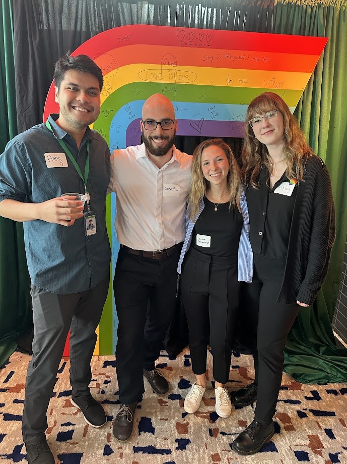 With colleagues in front of a rainbow backdrop at an office Pride event