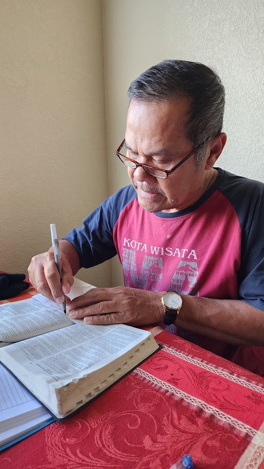 My father writing notes at the dining table with his Bible open