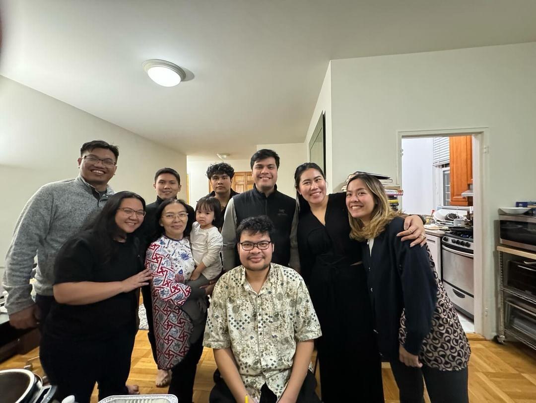 Everyone squeezed into a kitchen for a group photo, a toddler in her mother's arms