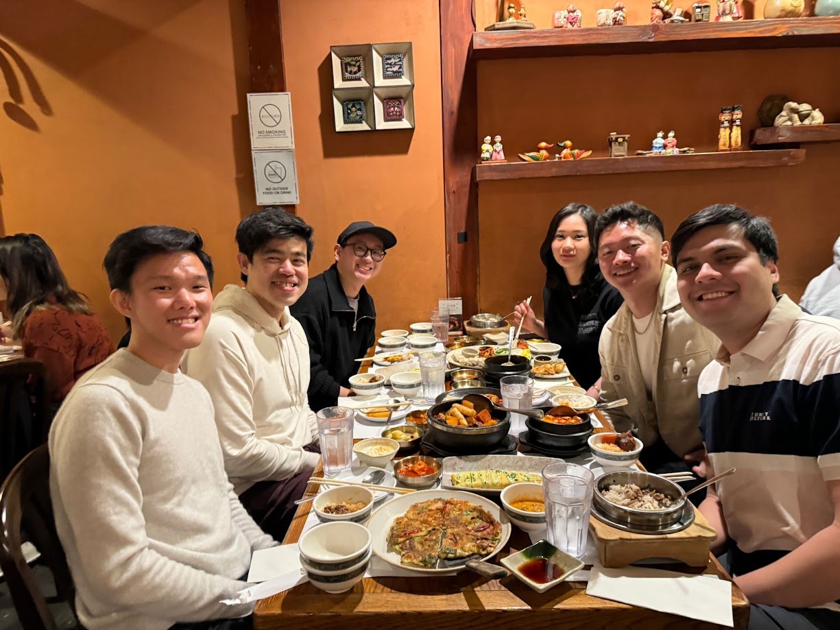 Six friends around a full Korean table, stone pots and pancakes between us