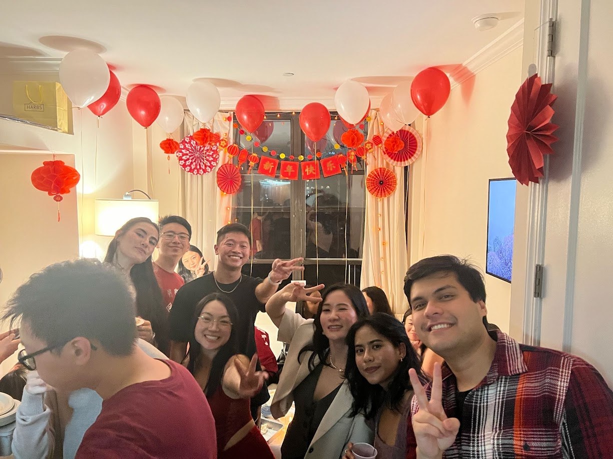 Crowded apartment party under red lanterns and a happy new year banner
