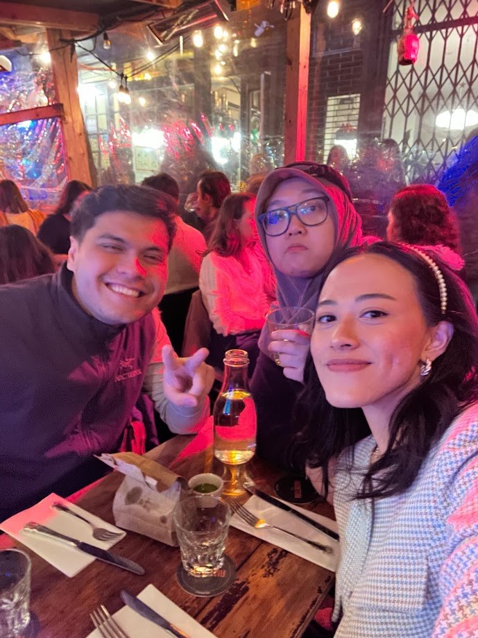Three of us at a long table under pink light