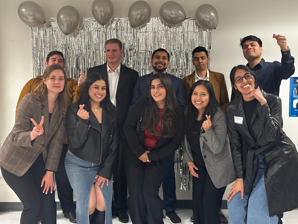 Group in business dress in front of a silver fringe backdrop and balloons