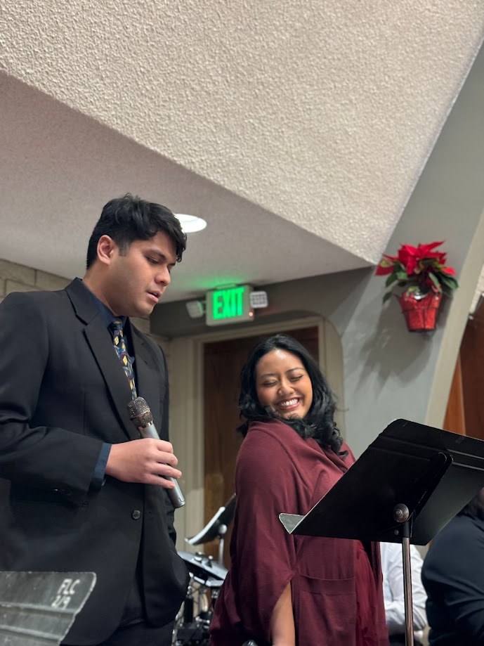 Singing from a music stand at church beside a friend, poinsettia on the wall