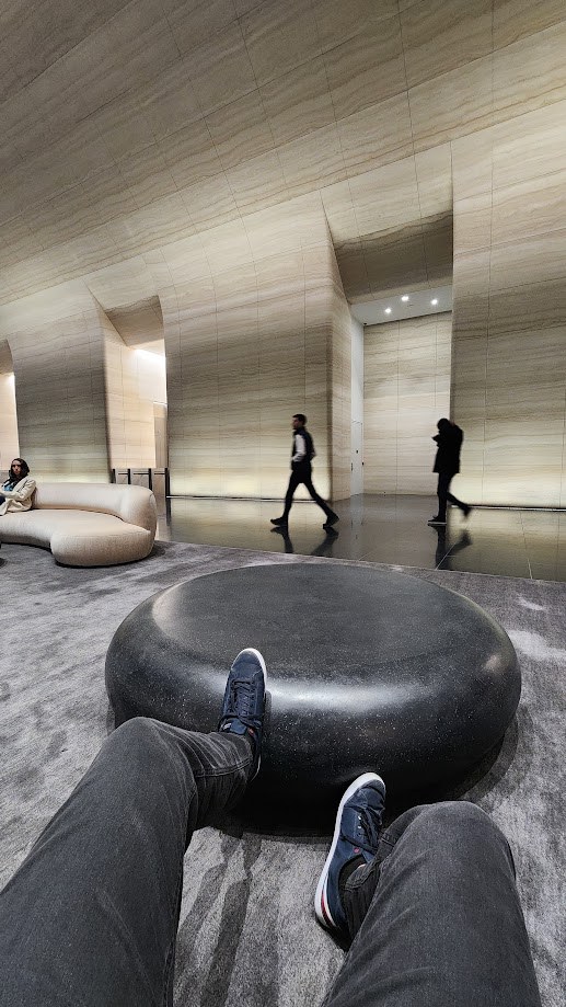 Feet up on a black stone seat in the lobby while people walk past