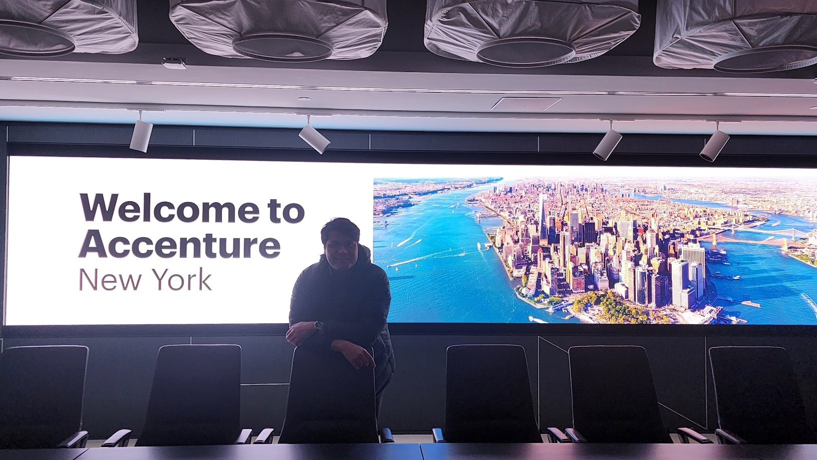 Standing in front of a wall screen reading Welcome to Accenture New York