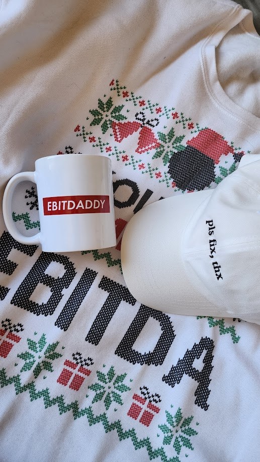 A gift set laid out: an EBITDA jumper, an EBITDADDY mug and a cap reading pls fix thx