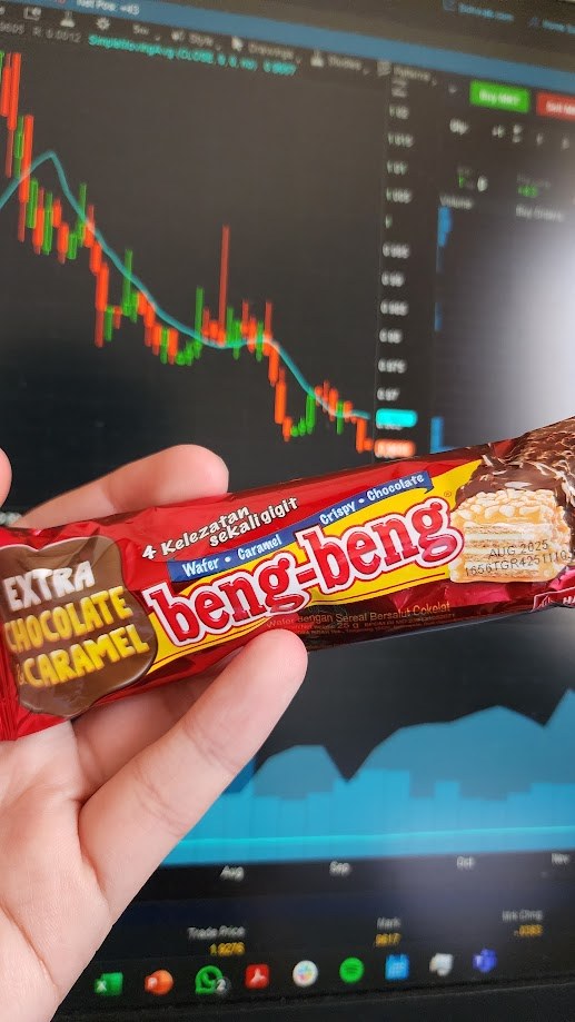 Holding a beng-beng bar in front of a screen of candlestick charts