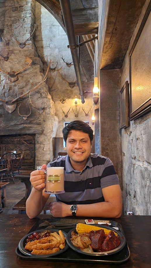 Holding up a butterbeer at a table of ribs and corn inside the Three Broomsticks