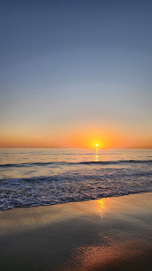 The sun going down over the ocean, the last of it reflected on the wet sand