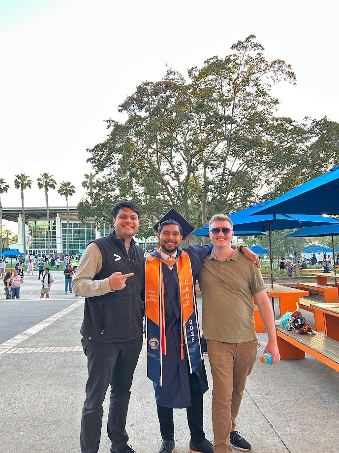 Three of us outside the CSUF 2025 commencement, one in cap, gown and stole