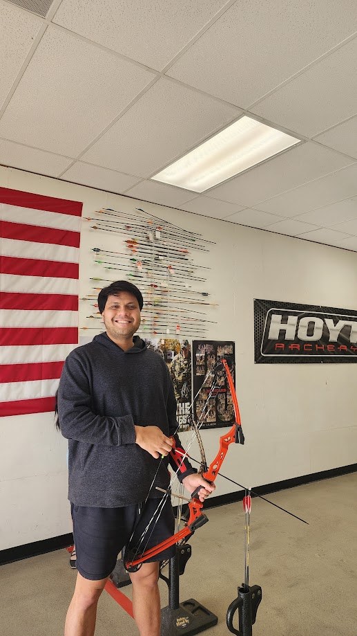 Holding a red compound bow at the archery shop