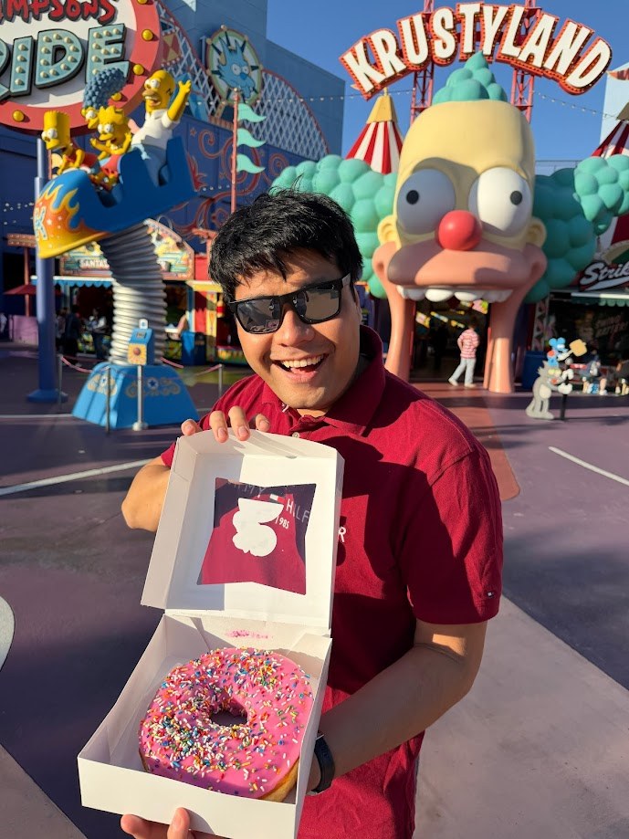 Holding open a box with a pink sprinkled donut in front of Krustyland