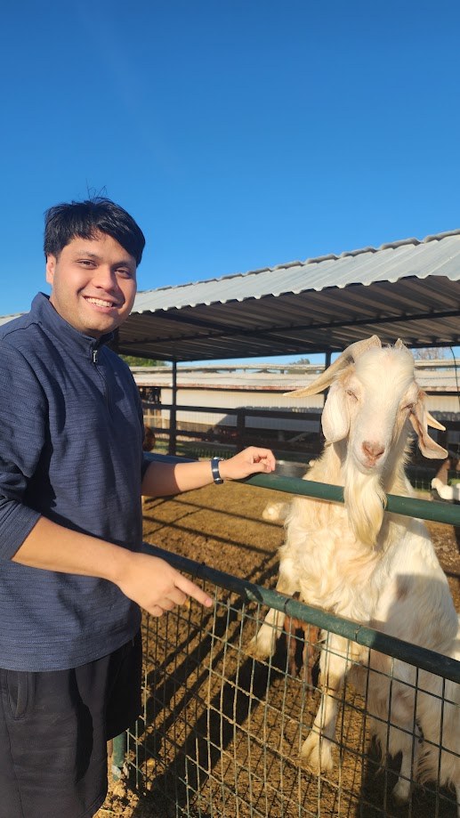 Standing at the fence with a goat leaning over it at the farm