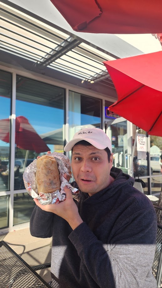 Holding up a foil wrapped burrito at an outdoor table