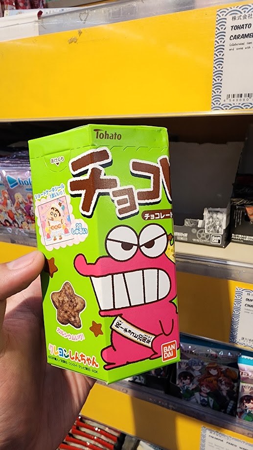 Holding a box of Crayon Shin-chan chocolate snacks in a Japanese snack shop